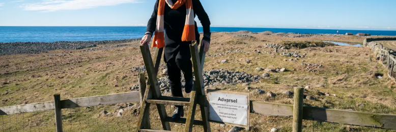 Formidler Elisabeth Søyland står på en gjerdeklyver forran strandgravfeltet på Hå gamle prestegard