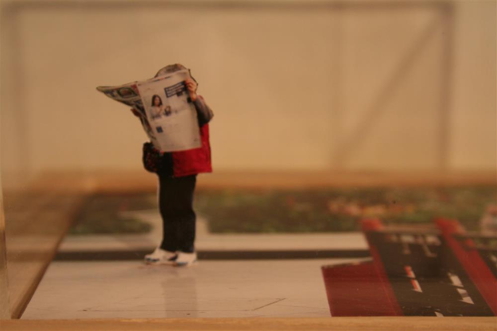 Installasjonsfoto. Kvinne i miniatyr som les avisa.  - Klikk for stort bilete