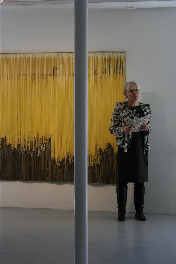Eva Watne opnar utstillinga. Står framfor ein gul og svart vevnad.  - Klikk for stort bilete